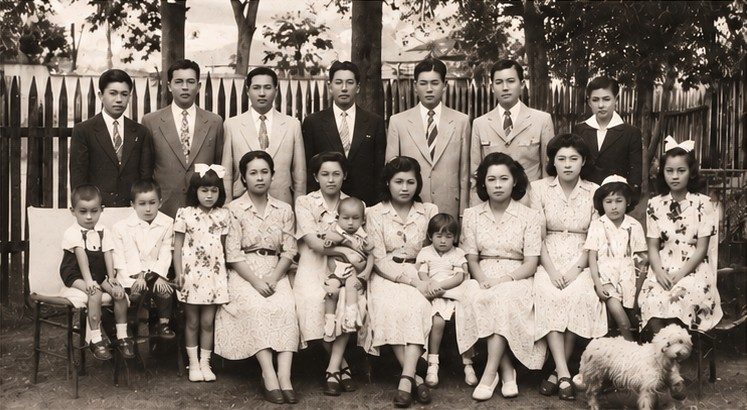Fotografia histórica em sépia da família de Kiroku Yanase: filhos, filhas, genros e netos reunidos em frente a uma cerca de madeira