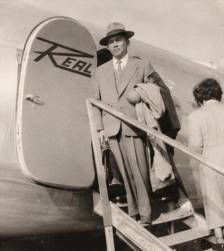 Fotografia histórica: Kiroku Yanase de terno e chapéu na escada de embarque de um avião da companhia aérea Real